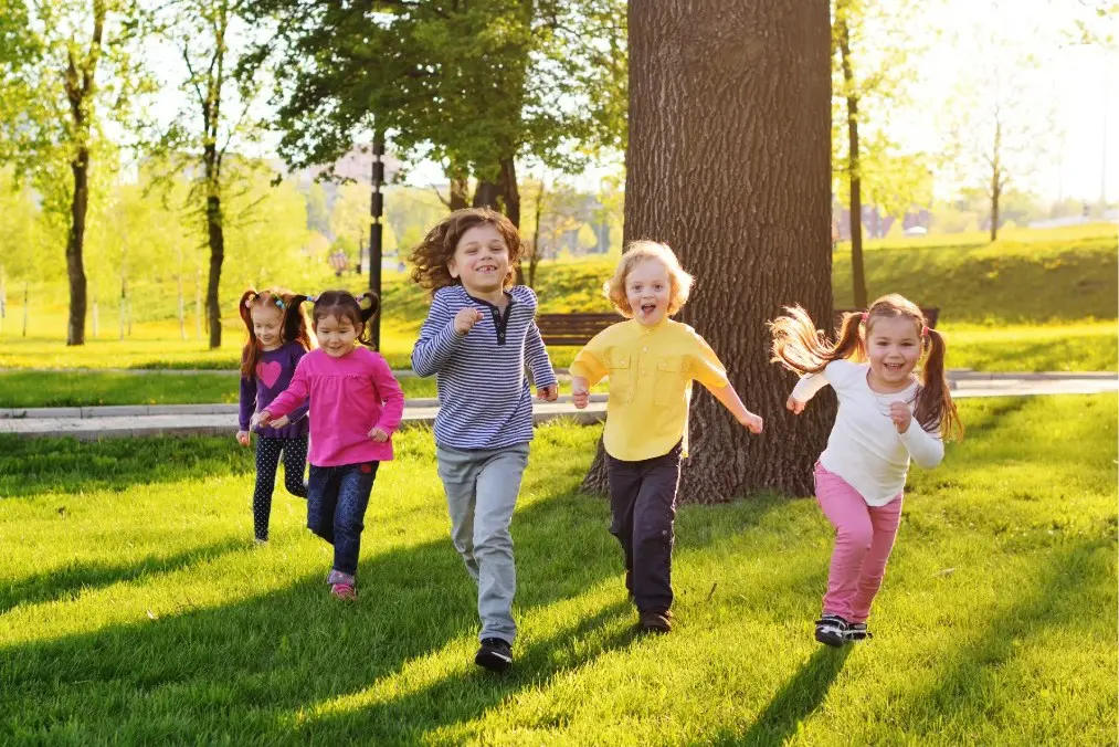 Group of active young children running and smiling across a sunny park lawn, representing the Early Observation SmileClub at Align Choice Orthodontics in Everett, WA.