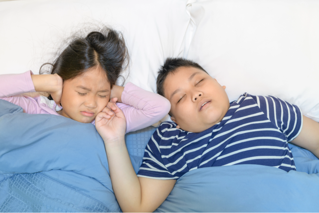 Child sleeping with mouth open snoring while sibling covers ears — signs of airway issues can be treated by Dr. Sogol, pediatric airway orthodontist in Everett, WA